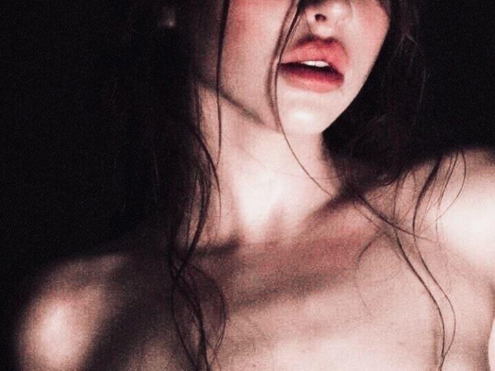 This may contain: a woman with red lipstick on her face and chest is posing for the camera in the dark