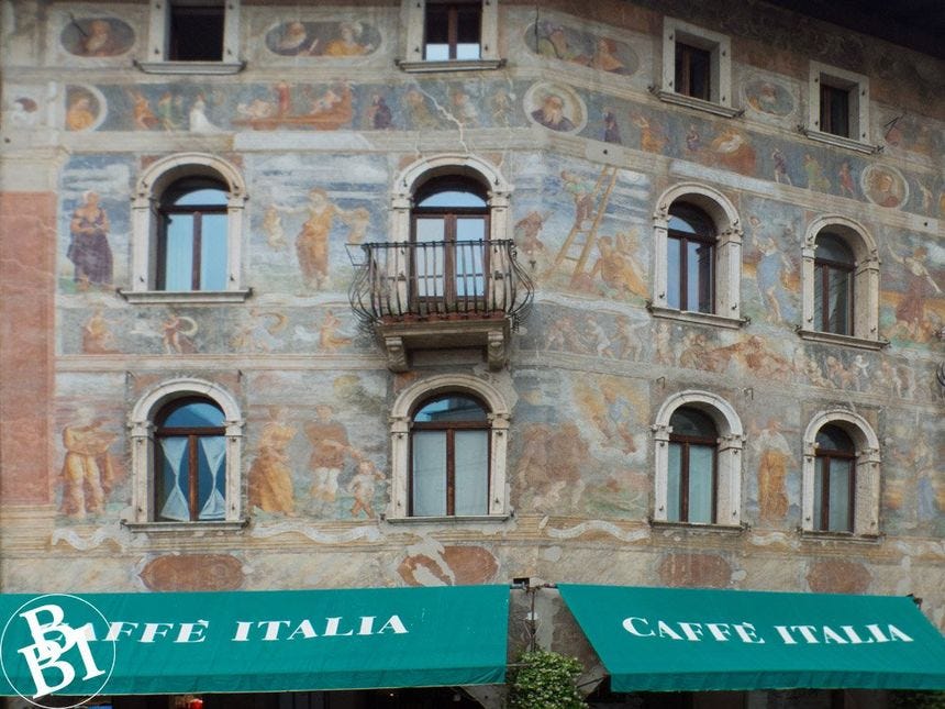 Outside of a building with frescoes and green canopies above a restaurant