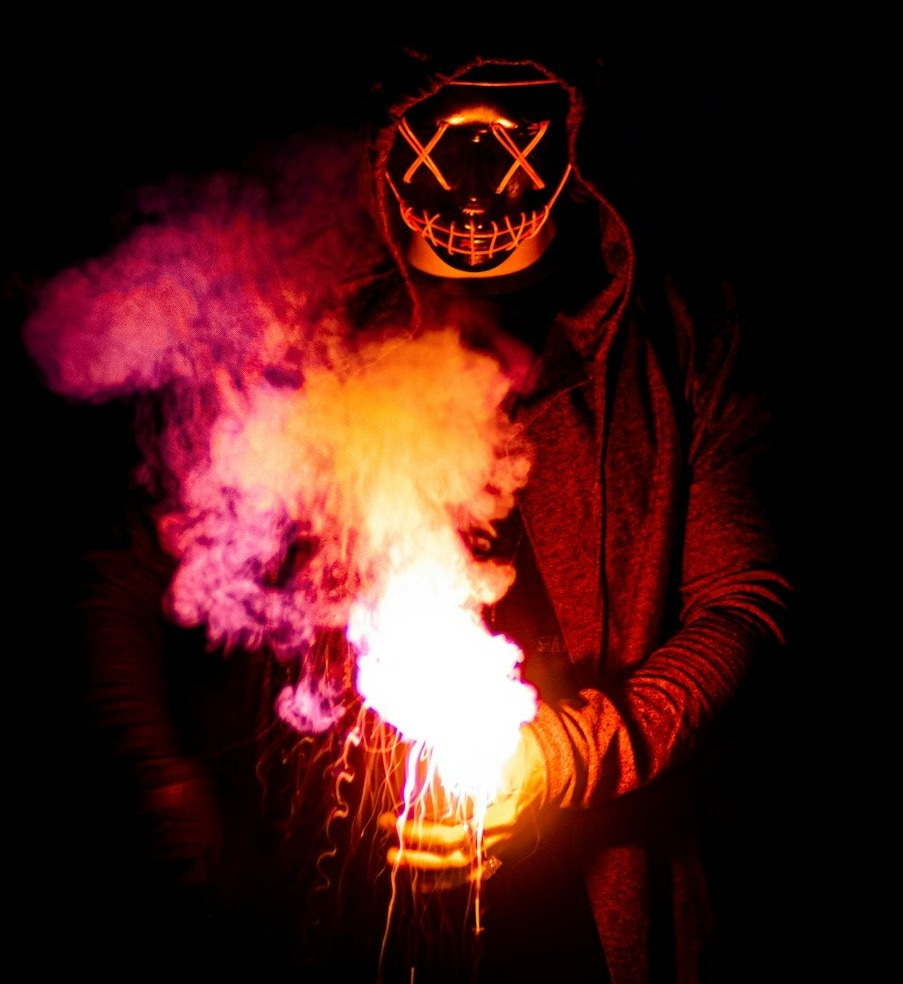 person in black mask holding purple and pink smoke person in black mask holding purple and pink smoke