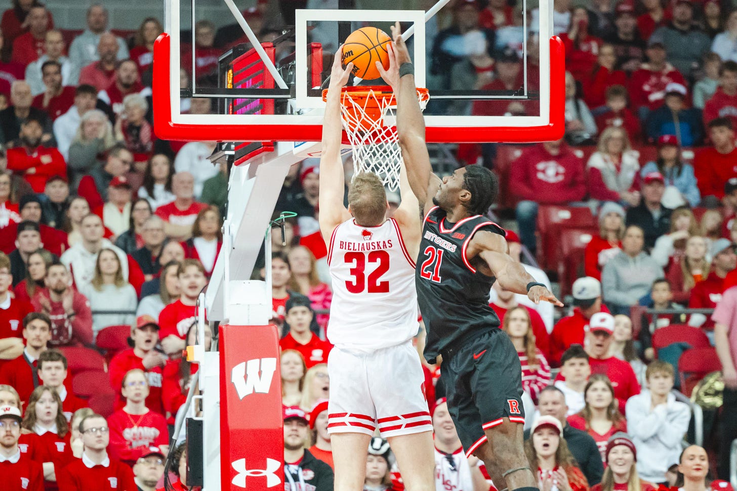 Facing toward the basket and away from the camera, Badgers basketball forward Aleksas Bieliauskas attempts a two-handed dunk over a defender