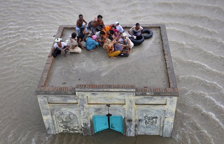 This may contain: several people sitting on top of an old building in the middle of flood waters with doors open