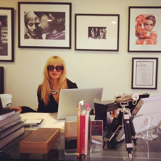 This may contain: a woman sitting at a desk with a laptop in front of her and several pictures on the wall behind her This may contain: a woman sitting at a desk with a laptop in front of her and several pictures on the wall behind her