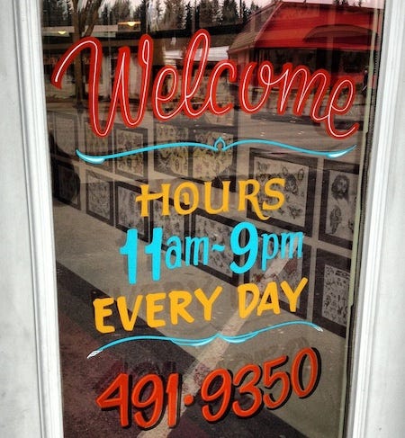 Hand-painted signage on a glass door reads: Welcome, with opening hours and phone number