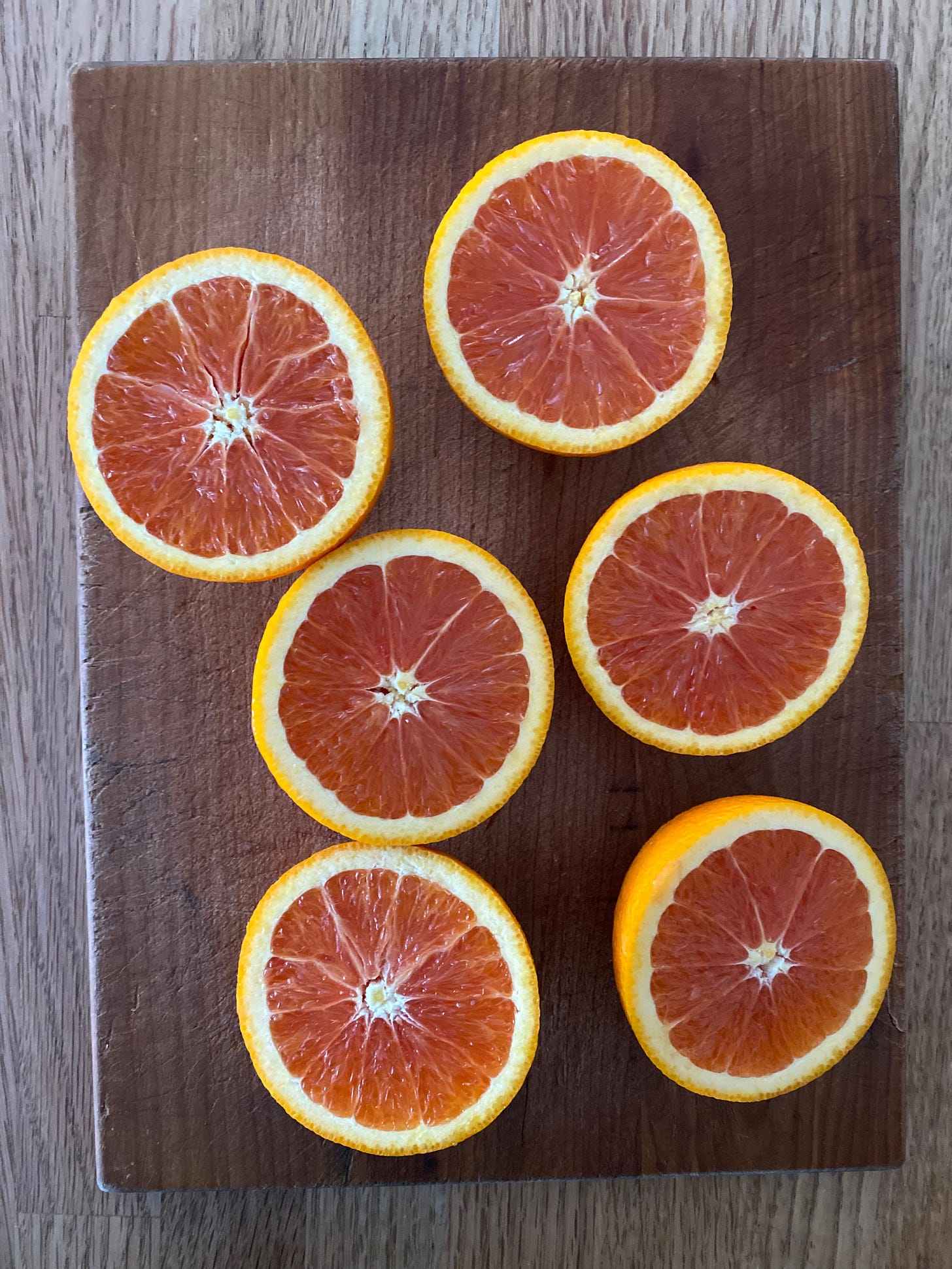Six halved cara cara oranges arranged on a wooden cutting board.