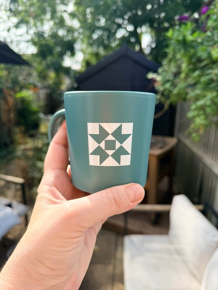 A teal mug with a patchwork motif and the words' The Clearing' in white