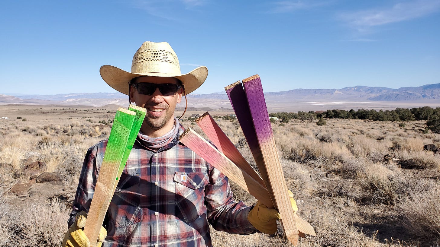 Eric holding wooden stakes with spray painted ends in green and purple for staking out the ground.