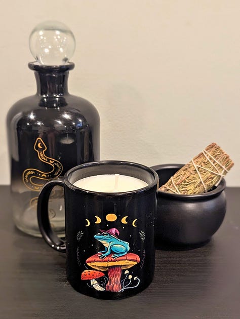 A gallery of candles made by The Chaos Kitchen including a red glass spiced cider, a lavender vanilla kitten mug, and a flower garden teacup.