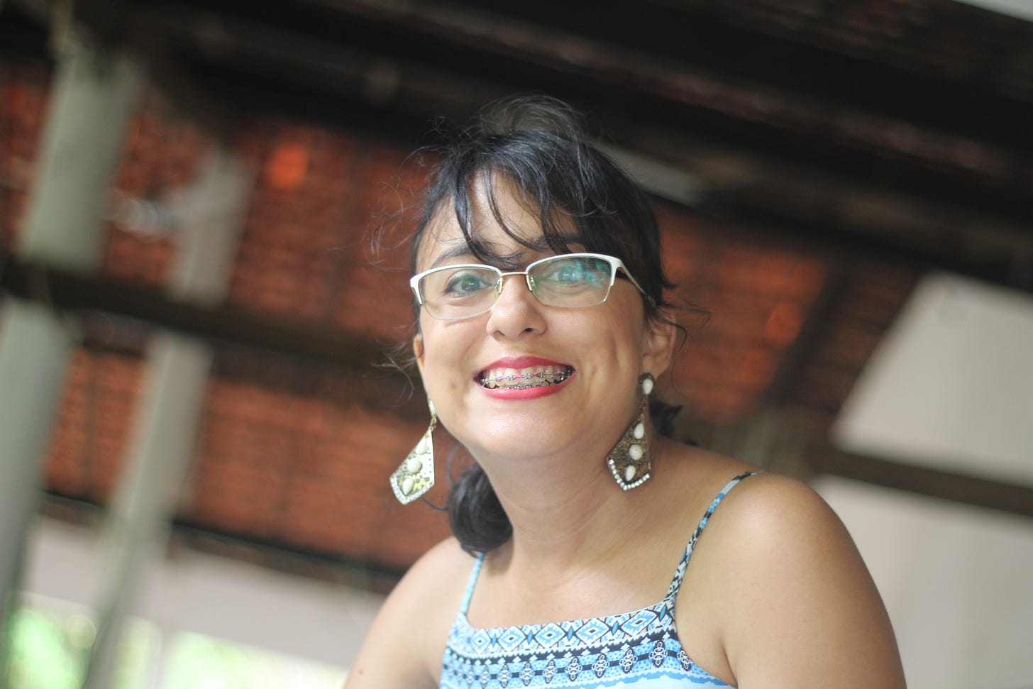 estou sorrindo, cabelos amarrados em um rabo de cavalo, brincos grandes, vestido azul estampado