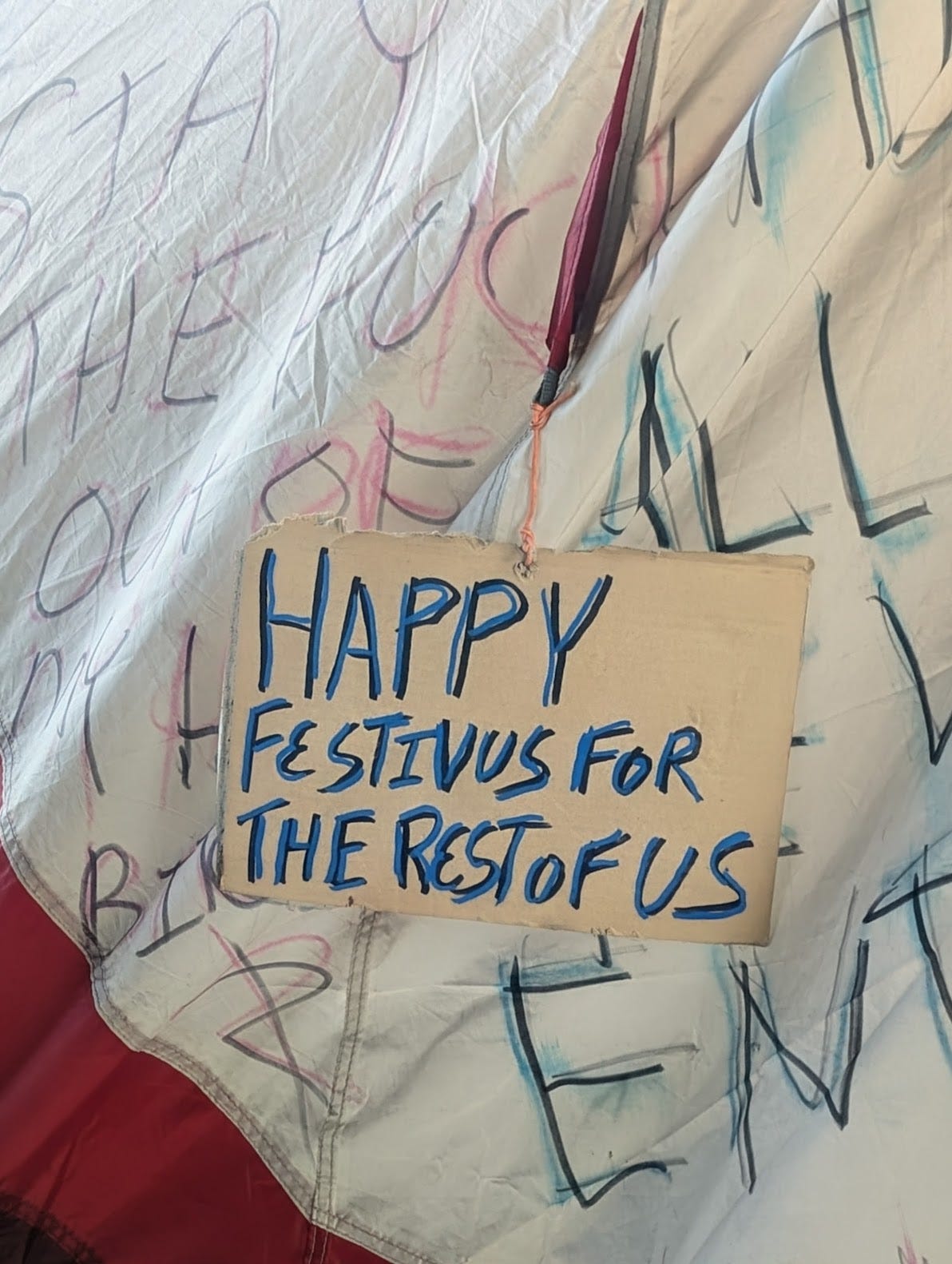 Handmade sign reading "Happy Festivus for the rest of us" affixed to a sidewalk tent.