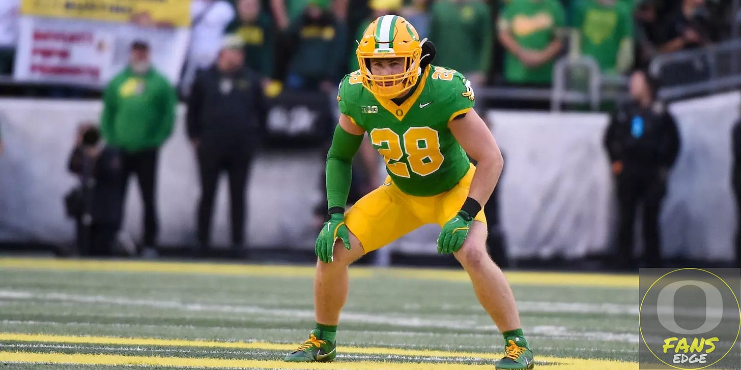 Oregon Ducks linebacker Bryce Boettcher wearing a green jersey with yellow pants, number 28, in a defensive stance on the field during a game. Fans and sideline staff are visible in the background.