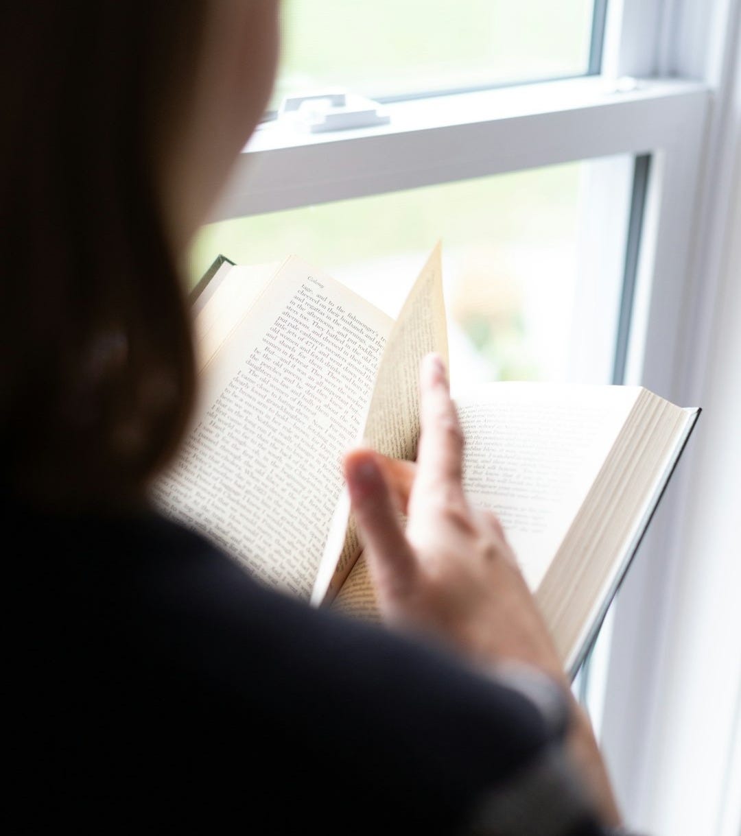 A woman reading a book by a window