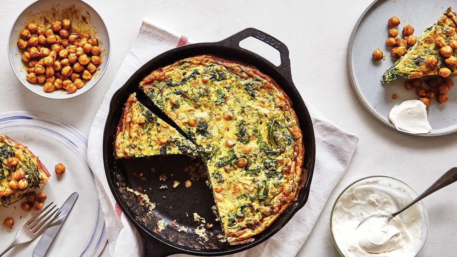Sliced frittata in cast iron skillet. To the sides a bowl of spiced chickpeas garlic mayonnaise and two plates with...
