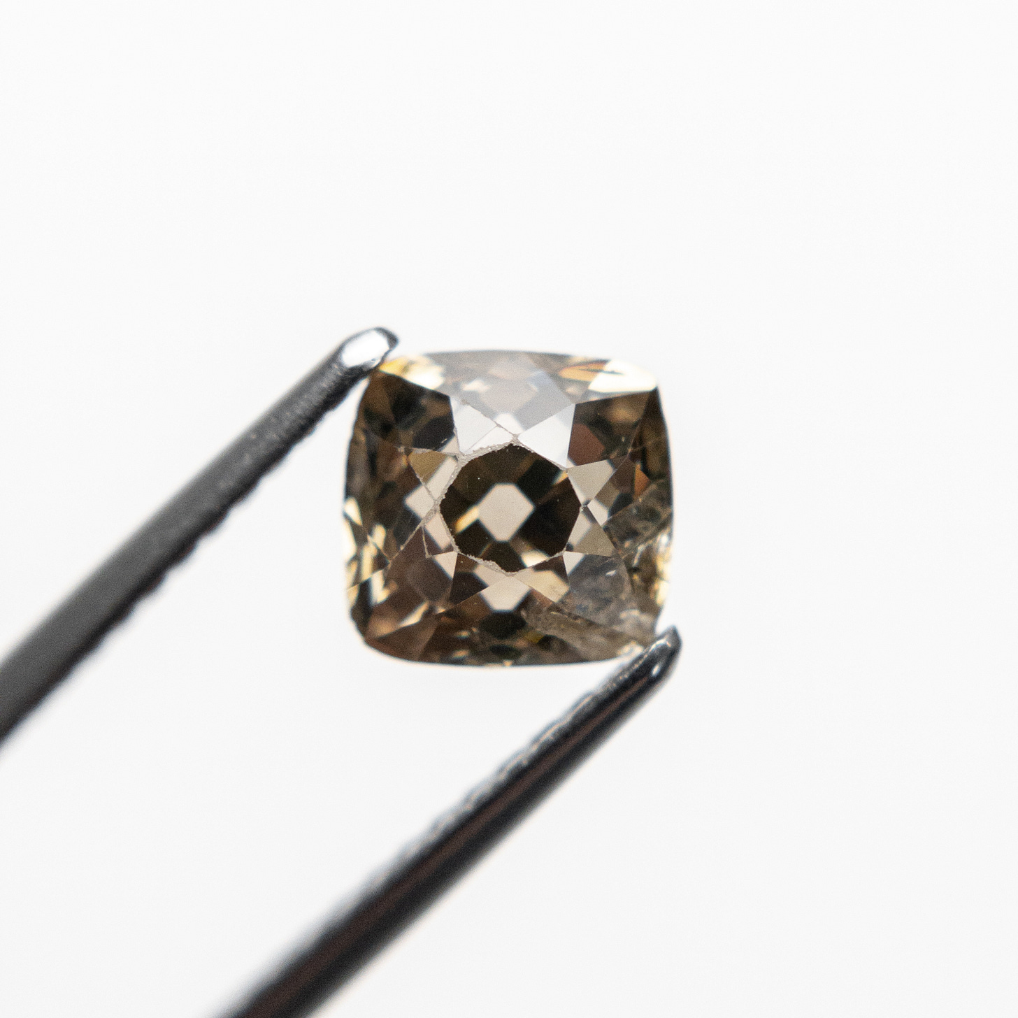 An antique cognac old mine cut diamond is held with diamond tweezers An antique cognac old mine cut diamond is held with diamond tweezers