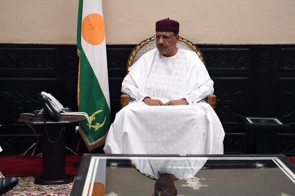 A man sits in a chair beside a flag of Niger. A man sits in a chair beside a flag of Niger.