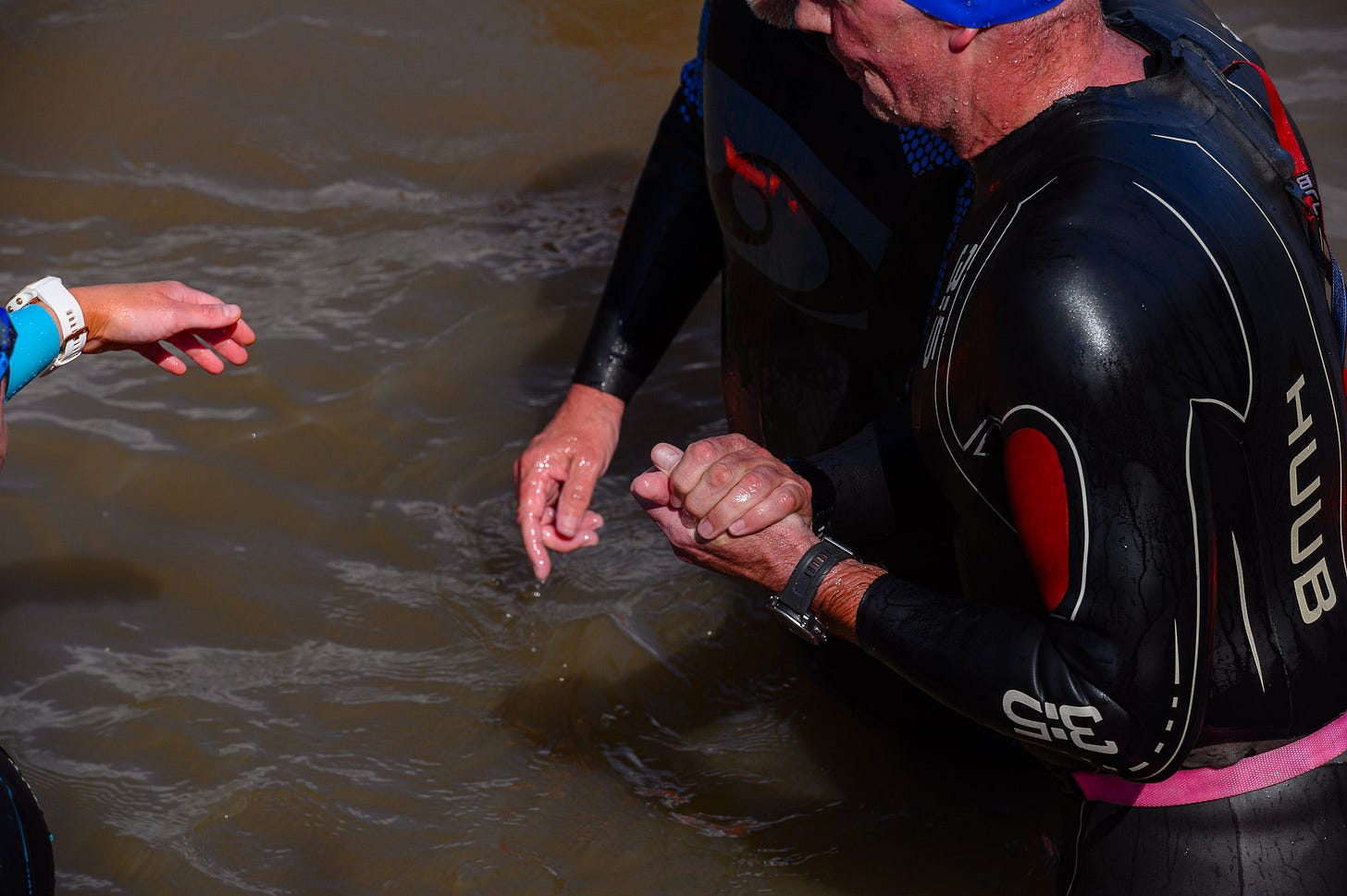 Two men hold hands for stability as they exit the water.