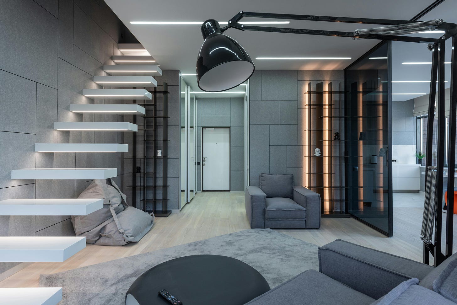 Modern living room with gray furniture, floating staircase, wall-mounted shelves, large floor lamp, glass doors, and neutral decor.