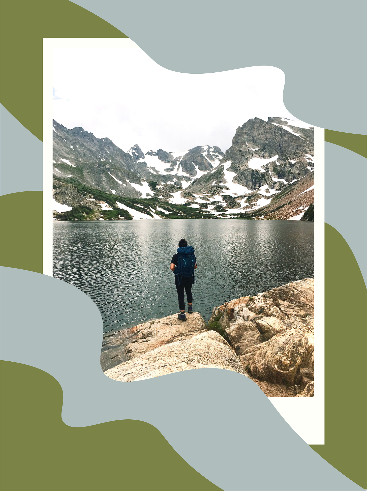woman wearing a hiking pack and looking out at an alpine lake with mountains dotted in snow in the background