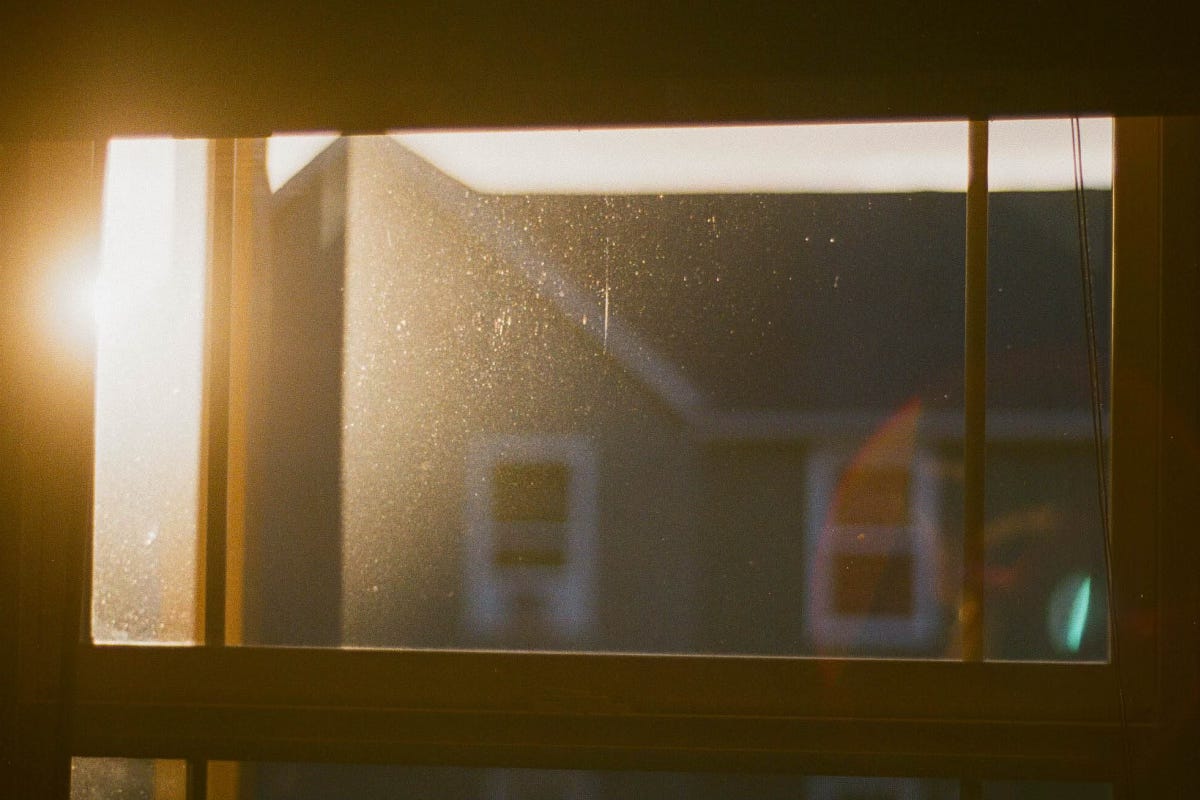 Dusty window looking out at the sun and a neighboring house