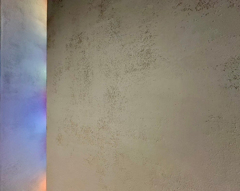 Close up of a textured white wall and roof that catches reflected pink, blue and pink light.
