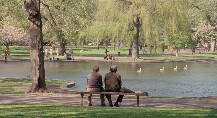 This may contain: two people sitting on a bench looking at the water in a park with swans and trees
