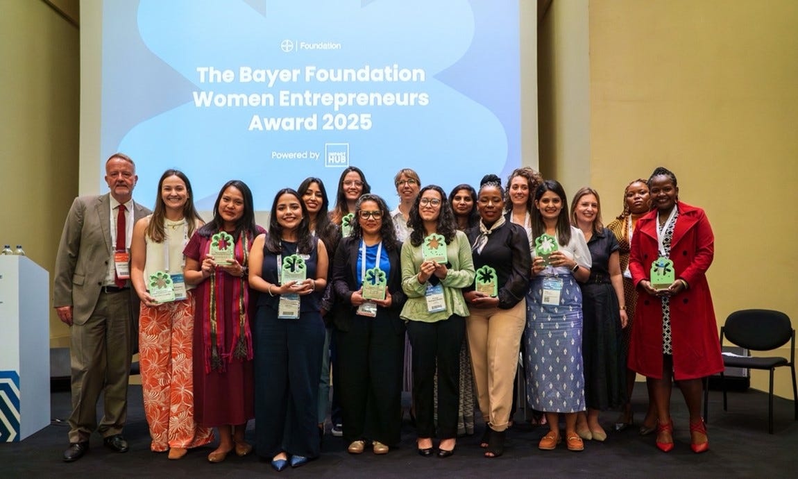 Group photo of fifteen winners of the Bayer Foundation Women Entrepreneurs Award 2025 standing on stage with their trophies, alongside event organizers, in front of a screen displaying the award title. Group photo of fifteen winners of the Bayer Foundation Women Entrepreneurs Award 2025 standing on stage with their trophies, alongside event organizers, in front of a screen displaying the award title.