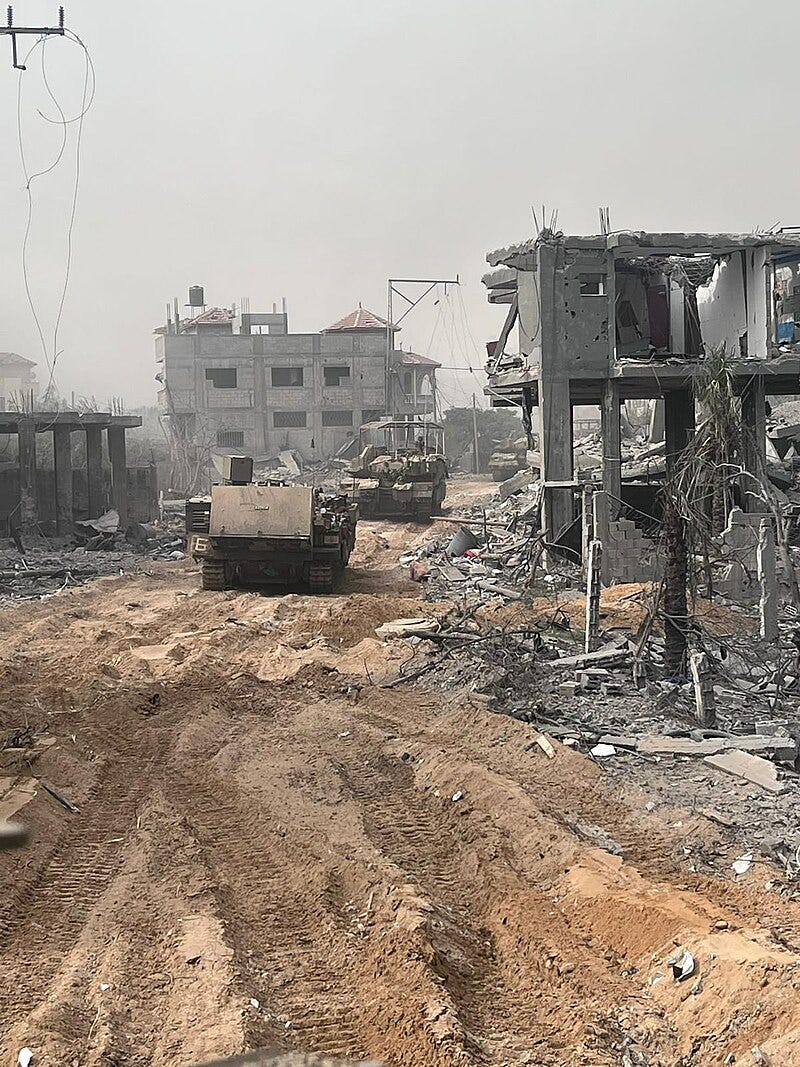 Two tanks roll on dirt, surrounded by a massive amount of destruction. There is rubble on the ground, and buildings that have been exploded Two tanks roll on dirt, surrounded by a massive amount of destruction. There is rubble on the ground, and buildings that have been exploded