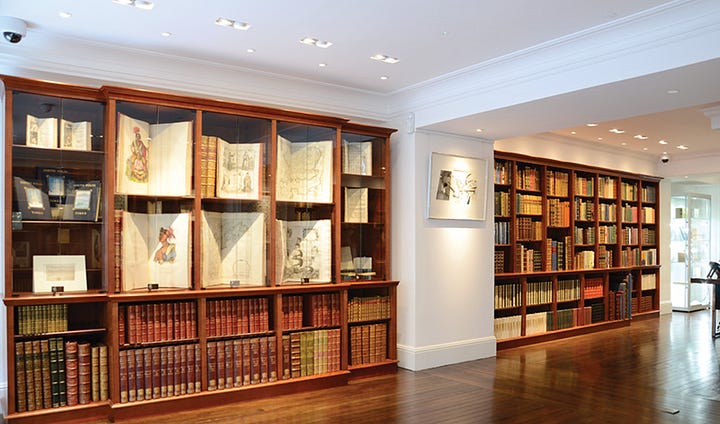 Interior gallery of Peter Harrington Rare Books in London. The first image shows a warm wood-paneled library with floor-to-ceiling mahogany shelves of leather-bound antiquarian books in red, green, and tan calf and morocco bindings, a glass-topped display cabinet of rare first editions, and a green-walled reading room beyond with a marble fireplace, oil portrait, and antique writing table. The second image shows a brighter showroom with tall glass-fronted display cases holding open antiquarian books, hand-colored maps, and illustrated plates above lower shelves of gilt leather-bound sets, with polished hardwood floors running into an adjoining room.