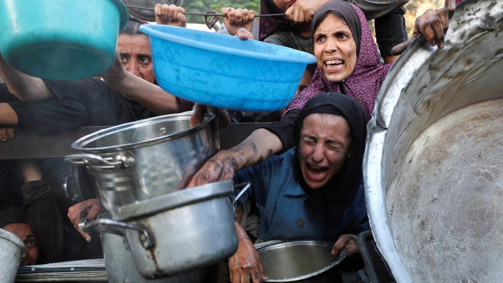 Palestinians react as they ask for food from a charity kitchen, amid a hunger crisis, in Gaza City, 14 on July 2025.