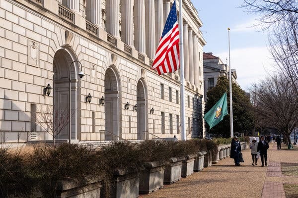People walking alongside a stone building and an American flag raised up on a pole. People walking alongside a stone building and an American flag raised up on a pole.