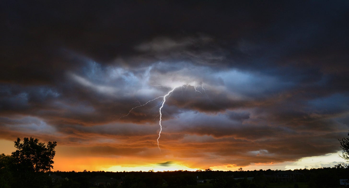 Dark storm clouds with a lightning bolt reaching down and a swath of orange from the setting sun on the horizon