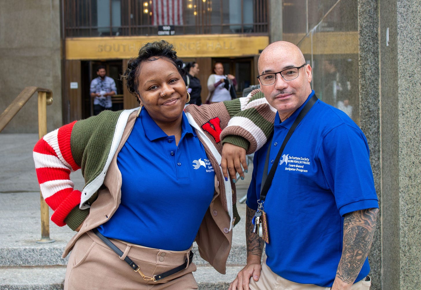 Two Fortune Society court navigators in blue program shirts stand together outside Manhattan Criminal Court.