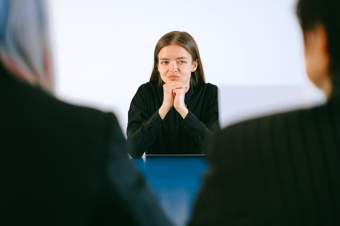 Woman in black blazer being interviews by two people across a blue table.