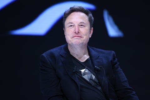 Elon Musk, in a dark blazer with a microphone on his lapel, smiles slightly during a discussion Elon Musk, in a dark blazer with a microphone on his lapel, smiles slightly during a discussion