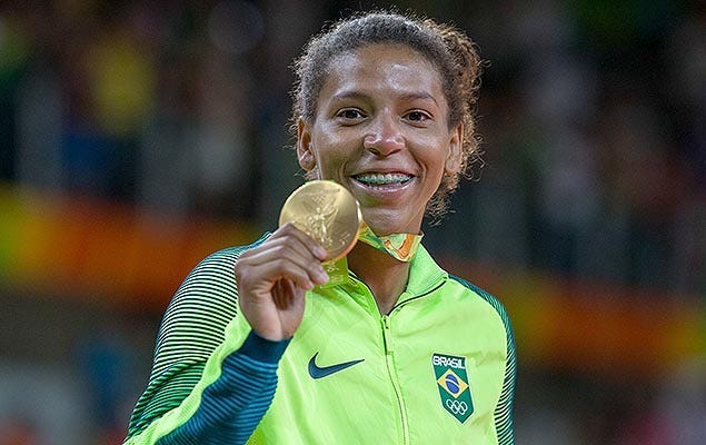 Foto da judoca Rafael Silva segurando medalha de ouro com um sorriso no rosto.