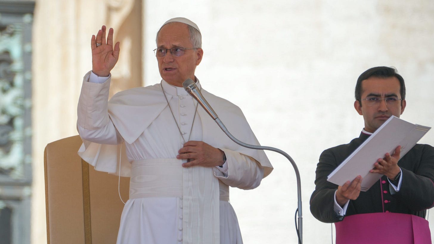 Pope Leo XIV raises his hand in blessing at the end of the general audience while an aide holds his papers Pope Leo XIV raises his hand in blessing at the end of the general audience while an aide holds his papers