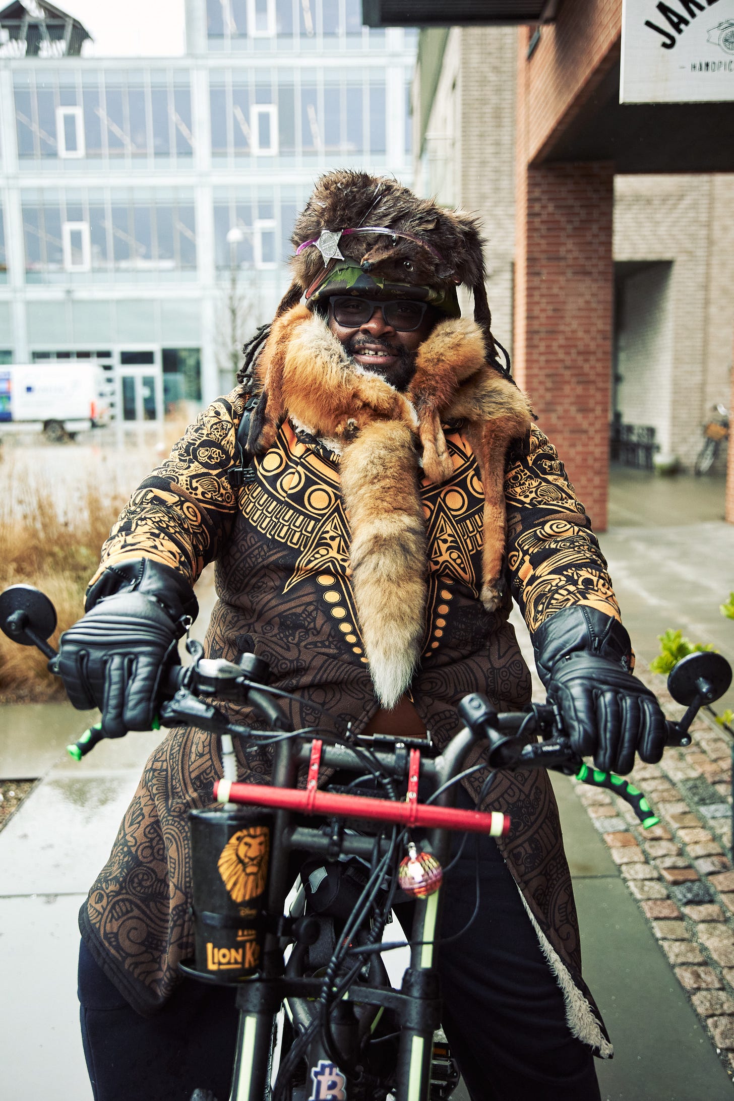 FatbikeHero (Tendai Frank Tagarira) performing in symbolic fur and patterned ceremonial attire while riding a fatbike in Aarhus, Denmark, as part of his AI-Critical performance art practice. FatbikeHero (Tendai Frank Tagarira) performing in symbolic fur and patterned ceremonial attire while riding a fatbike in Aarhus, Denmark, as part of his AI-Critical performance art practice.