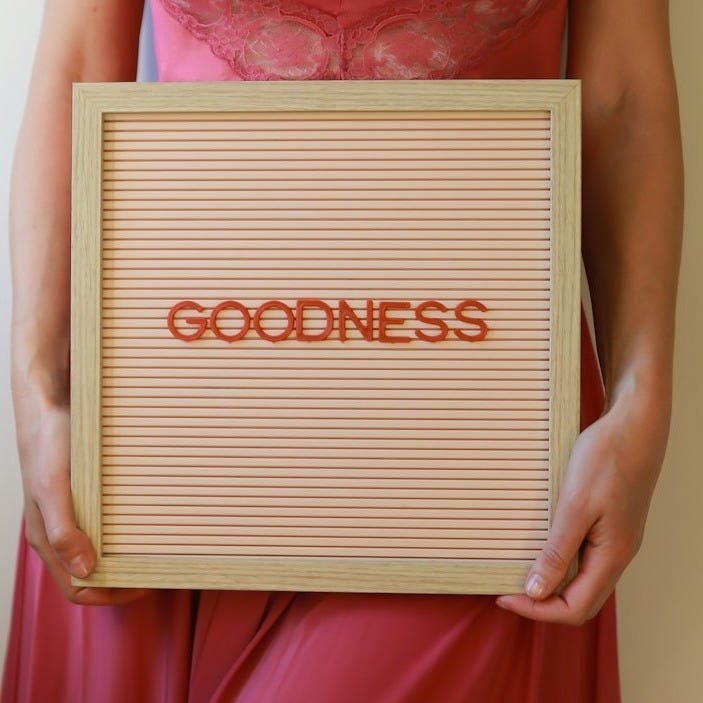 A woman holds a sign that says "goodness".