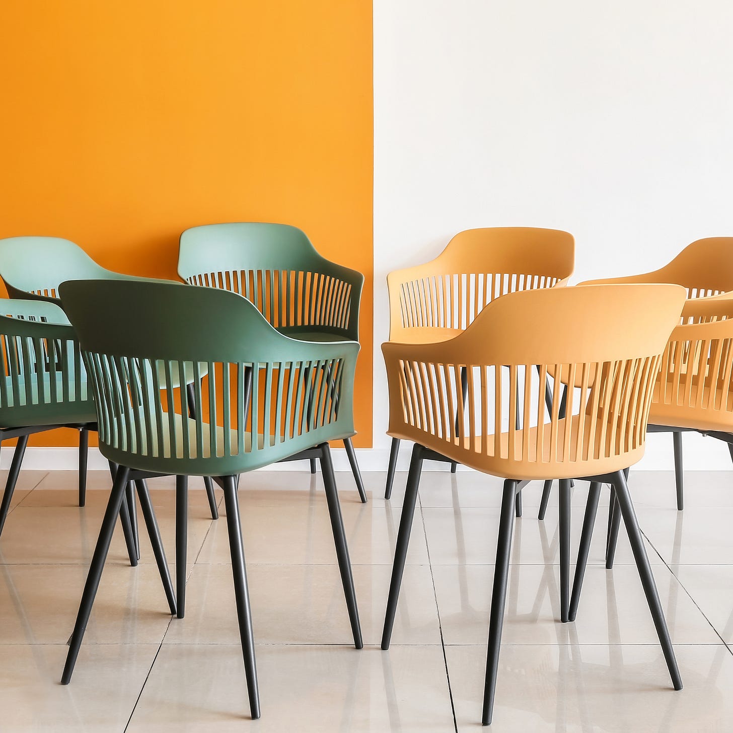Colorful plastic chairs arranged in a loose circle against an orange and white wall, with no people in sight.