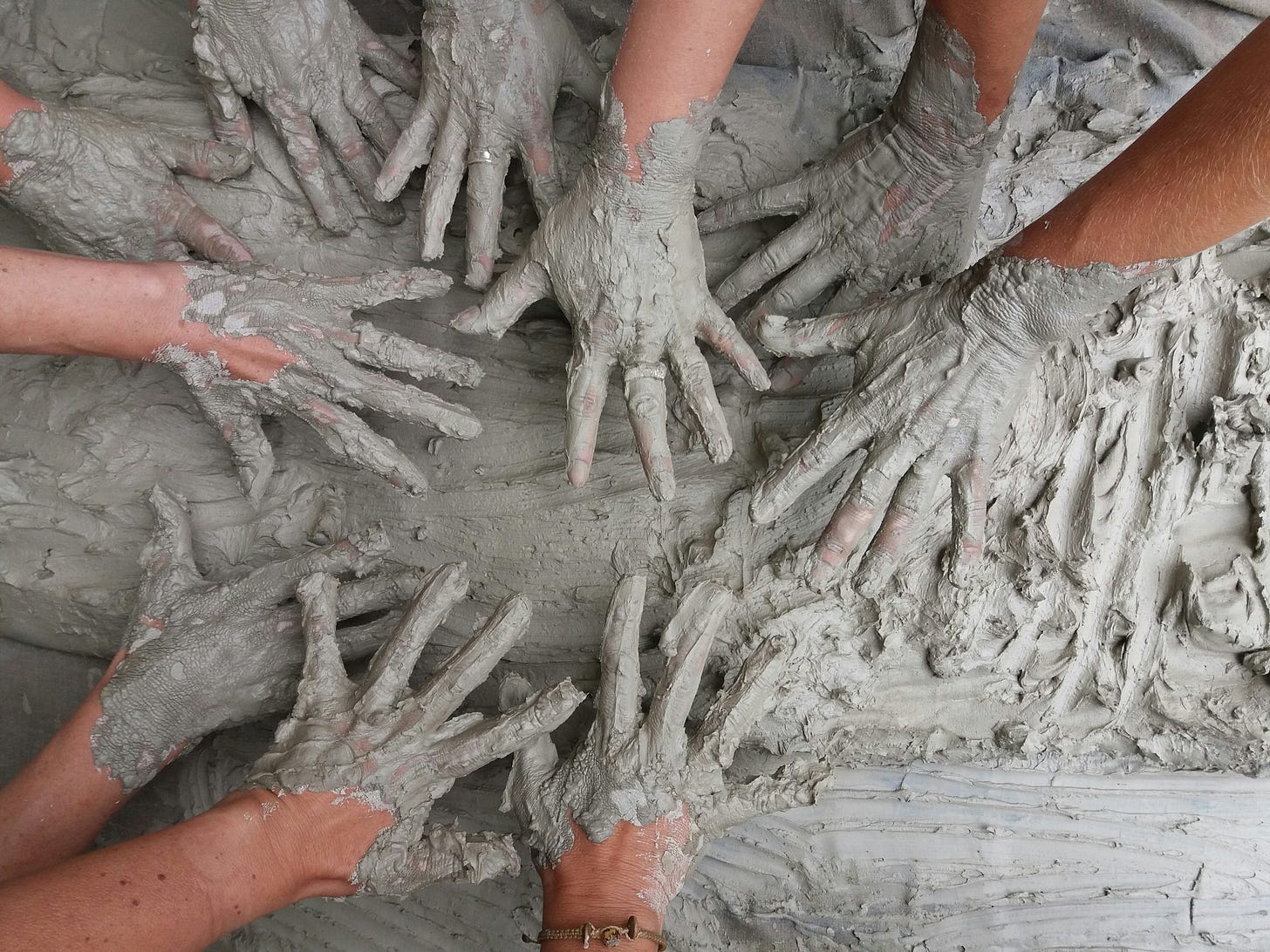 Many hands covered in wet clay
