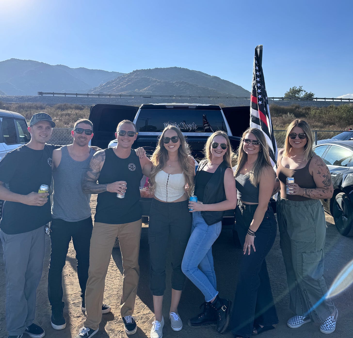 A group of grinning Creed fans, the thin blue line flag on their truck