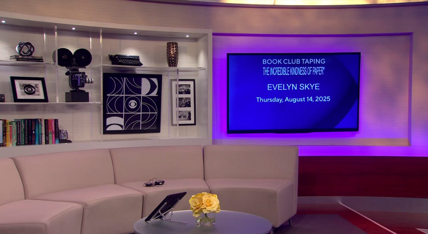 TV studio with long white couch, CBS logo in the background, and big screen showing info about the next segment to be taped, in this case: Evelyn Skye 