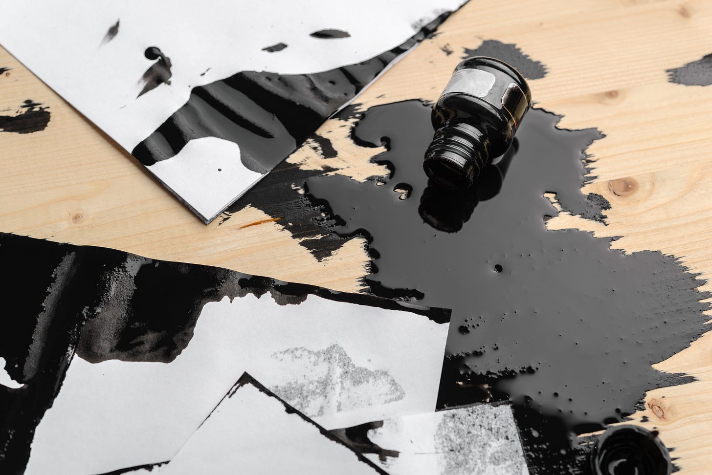 Ink bottle spilled onto paper and a wooden desk surface
