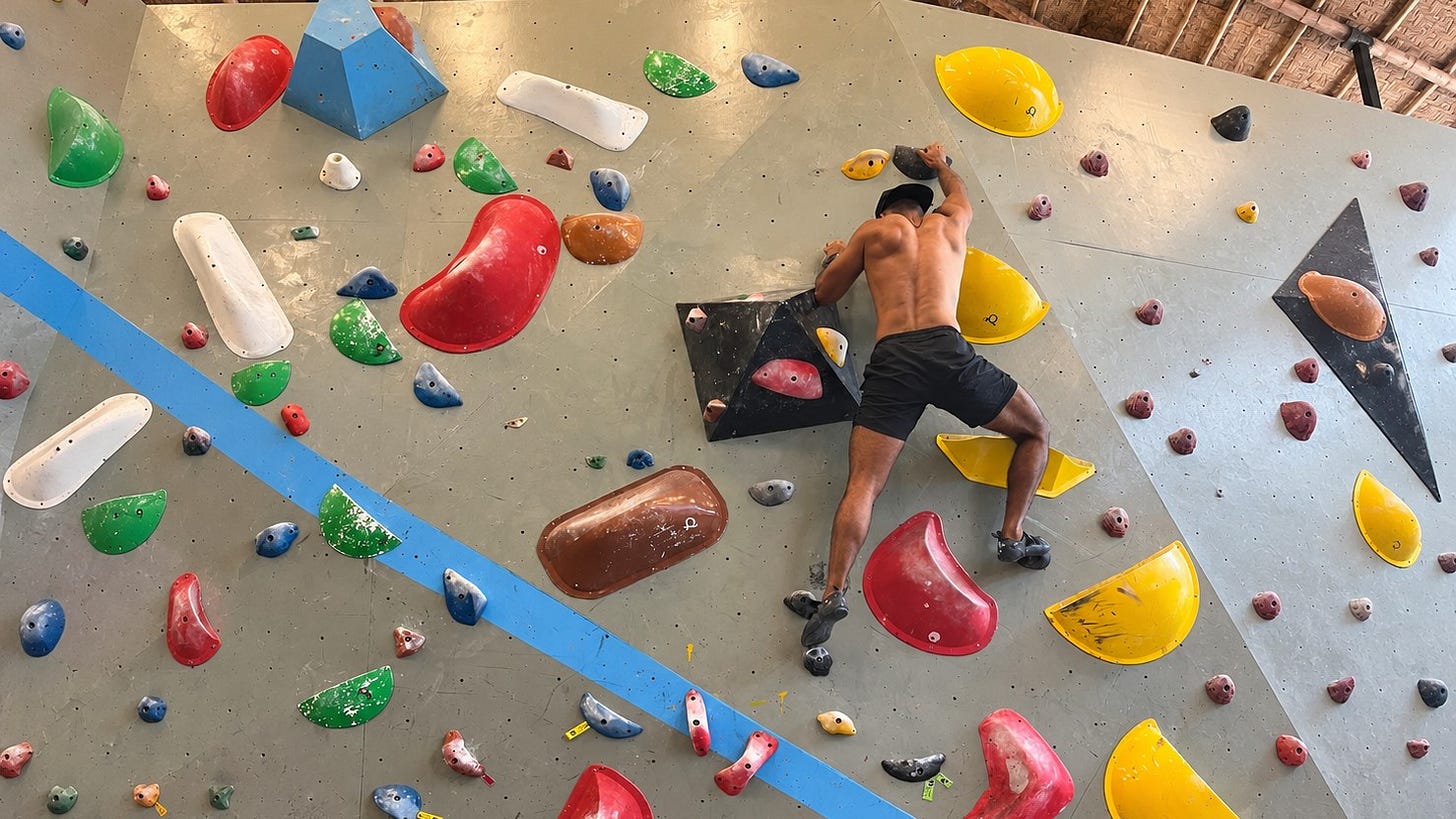 A climber mid-route on a bouldering wall, reaching for the next hold. A climber mid-route on a bouldering wall, reaching for the next hold.