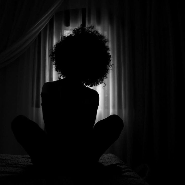 This may contain: a woman sitting on her bed in the dark This may contain: a woman sitting on her bed in the dark