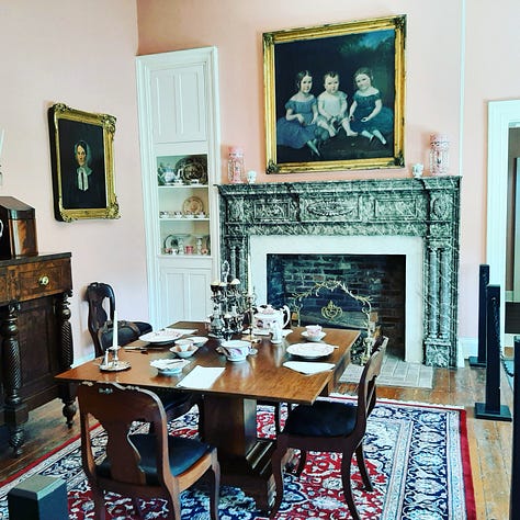 The Dickson Williams Mansion, a brick building with a white porch; the parlor, showing a round table surrounded by black chairs on a red oriental rug in front of a fireplace; the kitchen area, showing original north carolina furniture; bedrooms of the house, along with a portrait of General John Hunt Morgan sitting in a chair in a black coat with tall black boots; and the bed where he spent his last night.