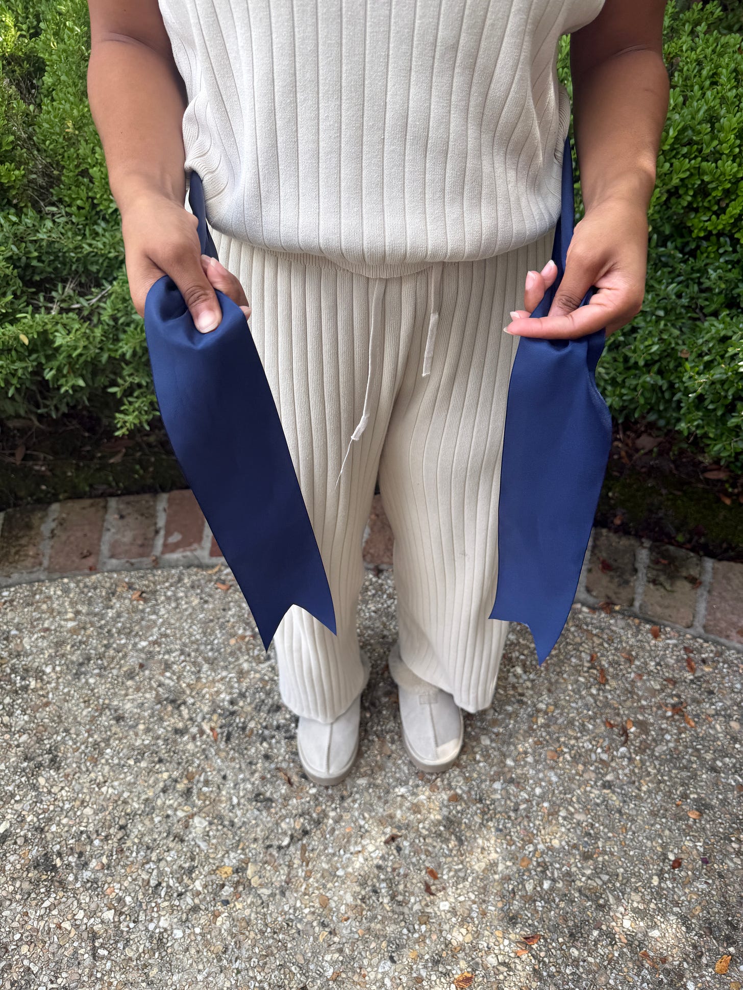 Hands positioning both ends of a navy ribbon at waist level, preparing to tie a bow