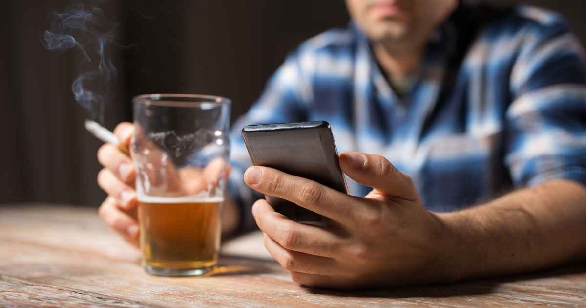 man with cell phone drinking alcohol and smoking