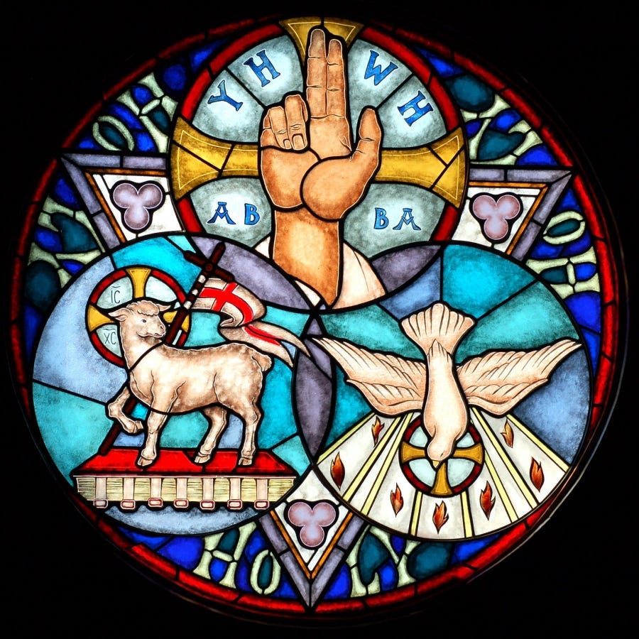 A stained glass depiction of the trinity featuring three interlocking circles with the raised blessing hand of the Father at the top, the Paschal lamb and flag symbolizing the Son, and the dove symbolizing the Holy Spirit. A stained glass depiction of the trinity featuring three interlocking circles with the raised blessing hand of the Father at the top, the Paschal lamb and flag symbolizing the Son, and the dove symbolizing the Holy Spirit.