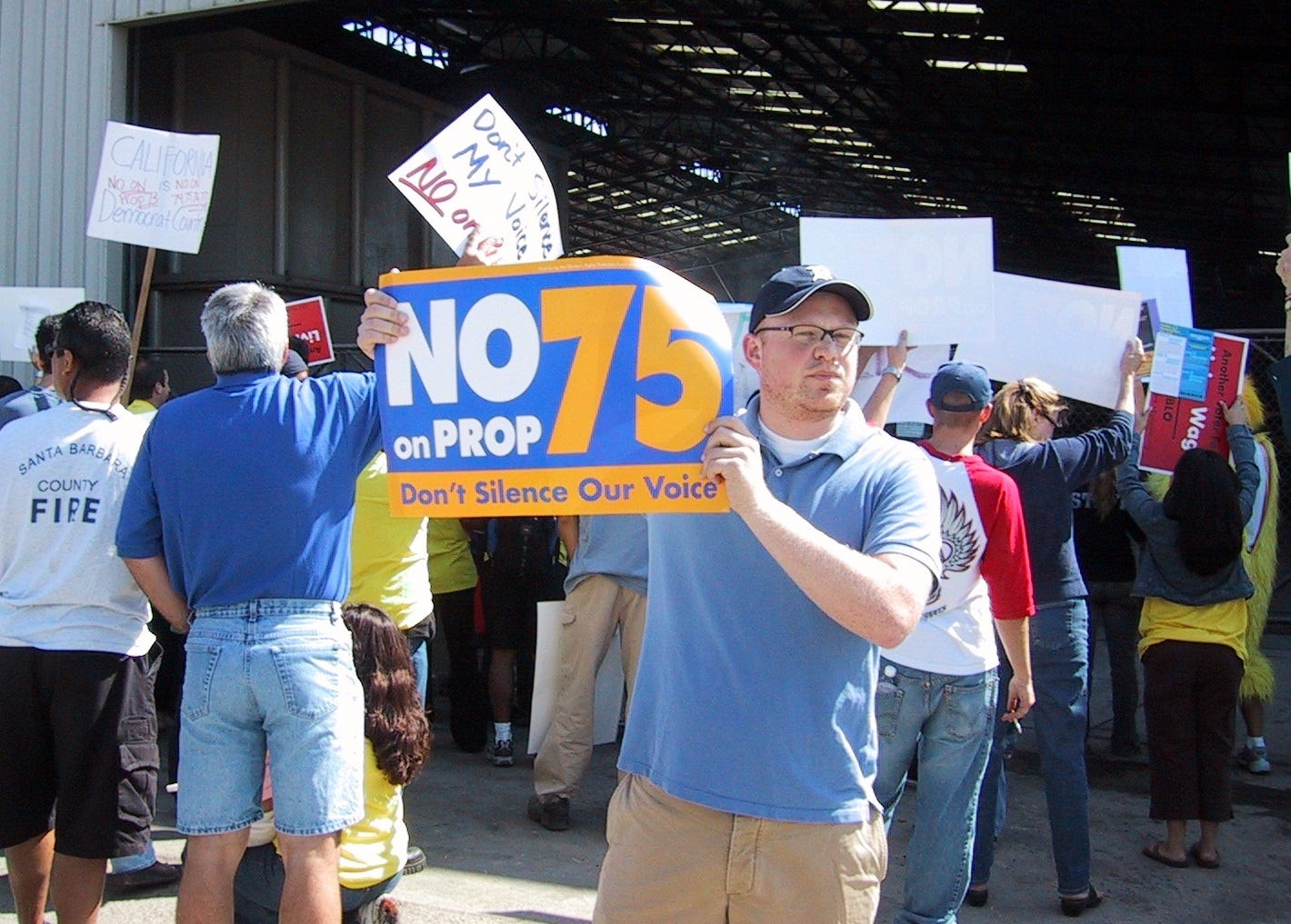 The author holding a protest sign "No on Prop 75, don't silence our voice" at a protest rally. The author holding a protest sign "No on Prop 75, don't silence our voice" at a protest rally.