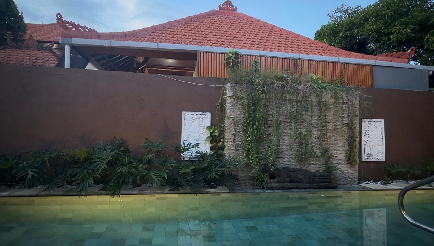 Concrete wall and temple roofline beside a Bali villa courtyard.